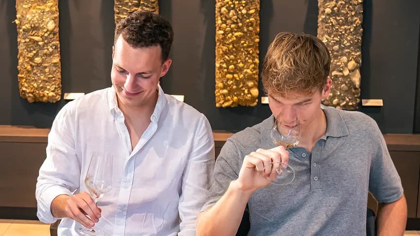 Two men tasting wine in a modern cellar.