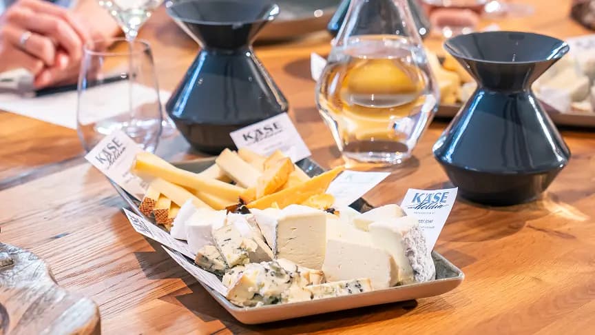 A platter of assorted cheeses and wine glasses on a wooden table.